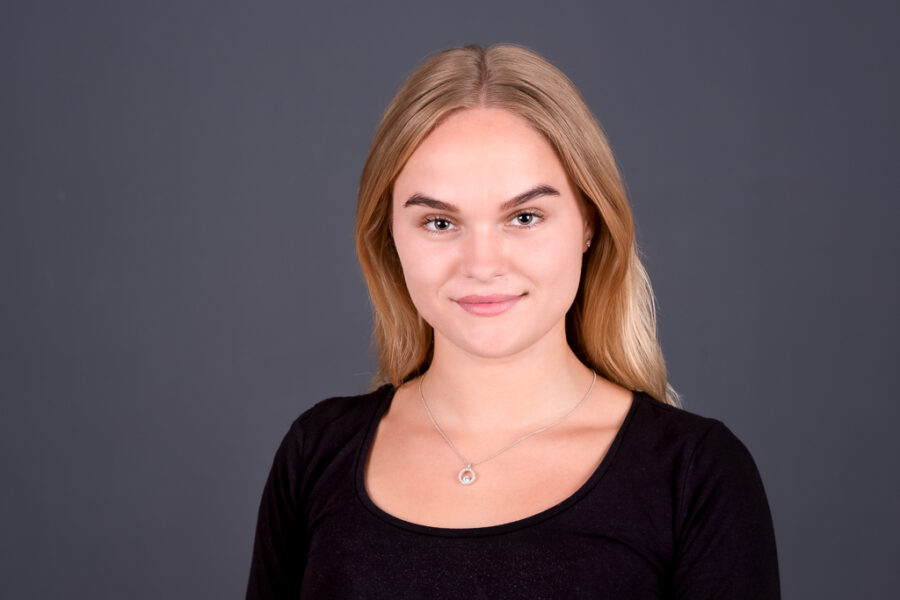 Porträt einer jungen Frau mit blonden Haaren Junge Frau mit blonden Haaren und einem schwarzen Oberteil vor einem grauen Hintergrund.