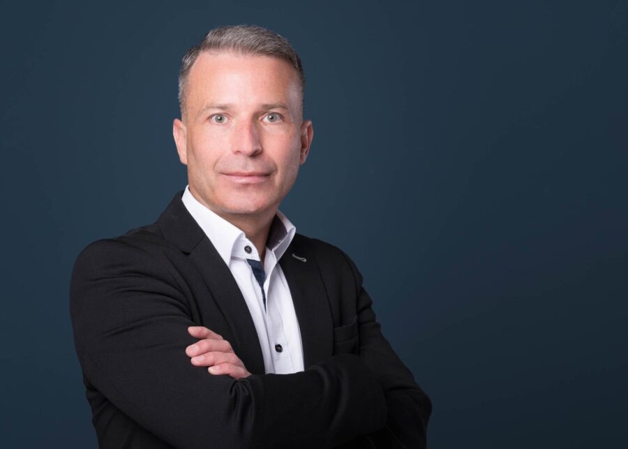 Porträt eines Mannes in Anzug mit verschränkten Armen Mann in einem schwarzen Anzug mit verschränkten Armen vor einem blauen Hintergrund.